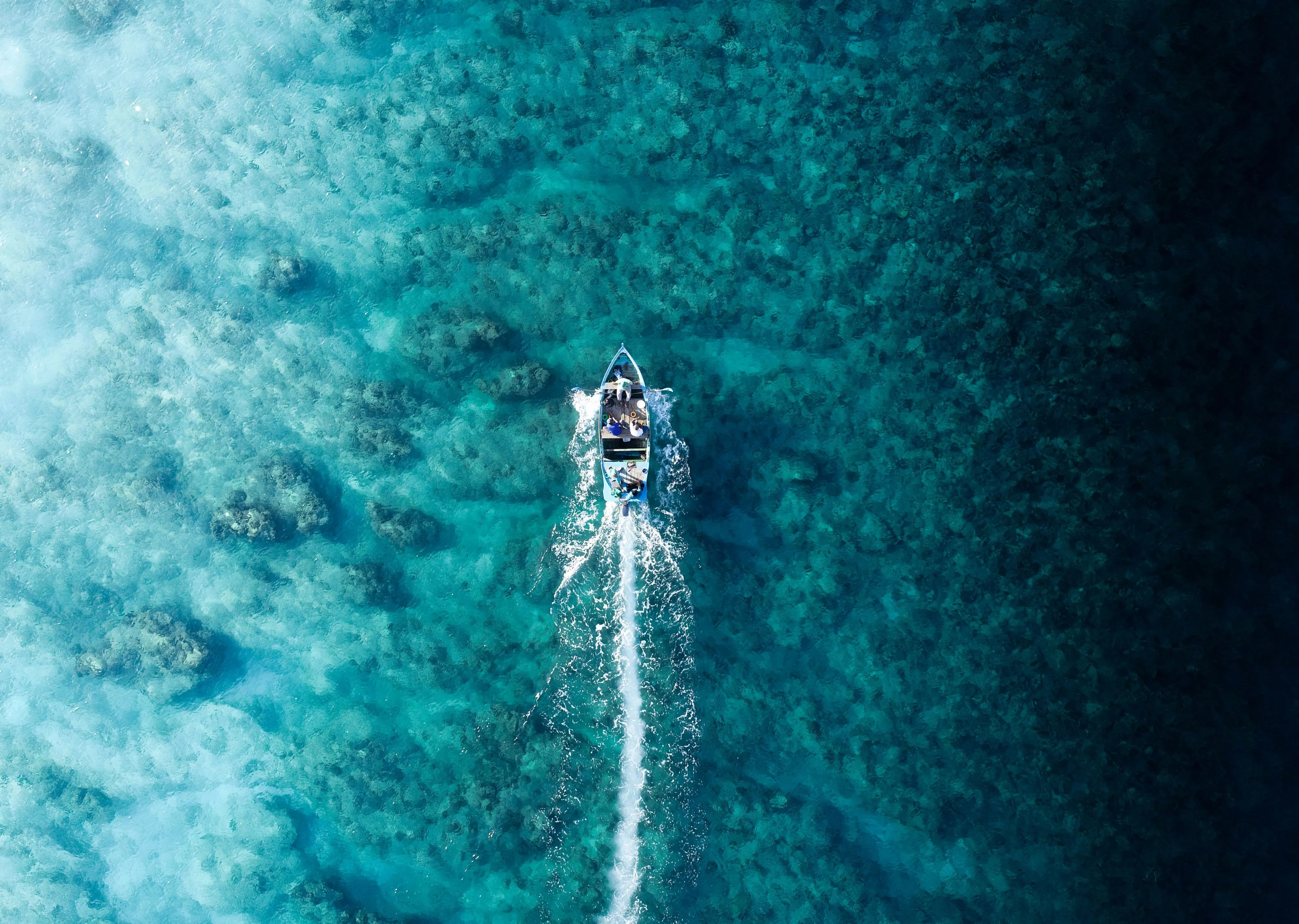 Aerial photo of a small motorboat traveling over clear turquoise water
